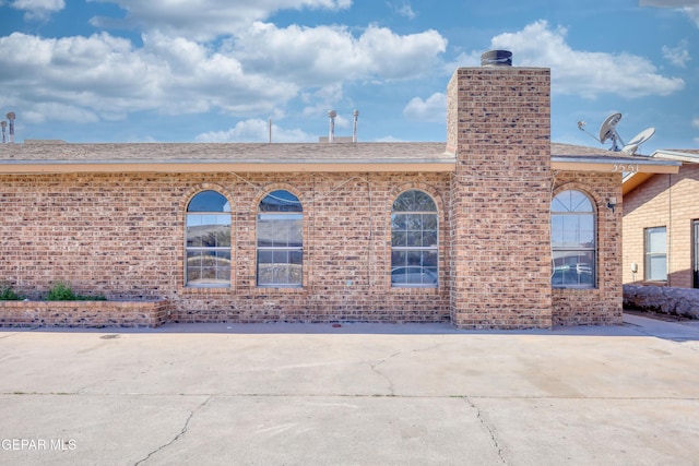 exterior space with a shingled roof, a patio area, brick siding, and a chimney