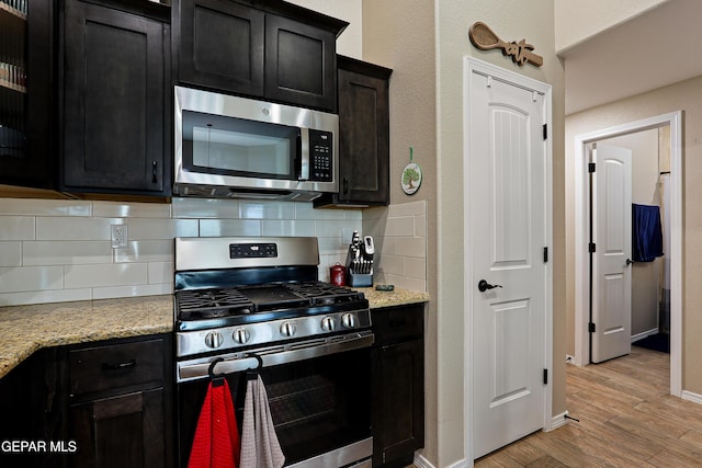 kitchen featuring stainless steel appliances, baseboards, light stone countertops, light wood finished floors, and tasteful backsplash