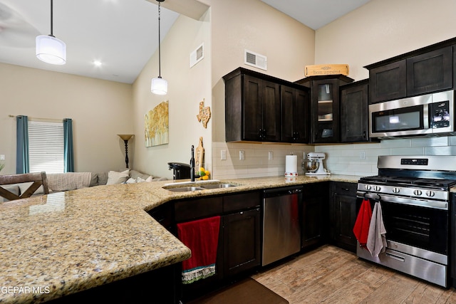 kitchen featuring visible vents, glass insert cabinets, decorative light fixtures, stainless steel appliances, and a sink