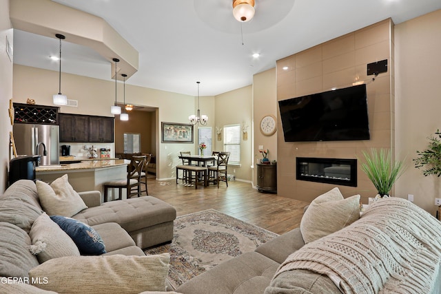 living area featuring light wood finished floors, a fireplace, baseboards, and ceiling fan with notable chandelier