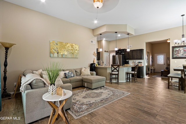 living room with dark wood-style floors, ceiling fan with notable chandelier, visible vents, and baseboards