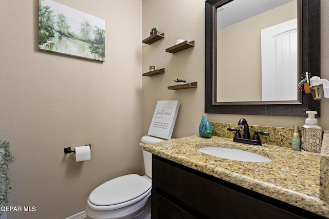 bathroom with toilet, a textured wall, and vanity