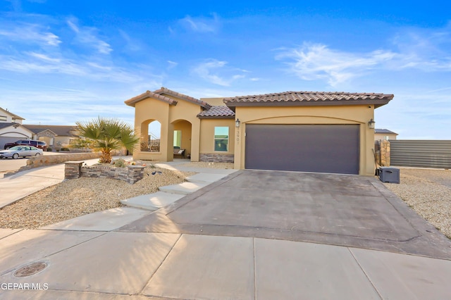 mediterranean / spanish-style house with a garage, concrete driveway, a tiled roof, and stucco siding