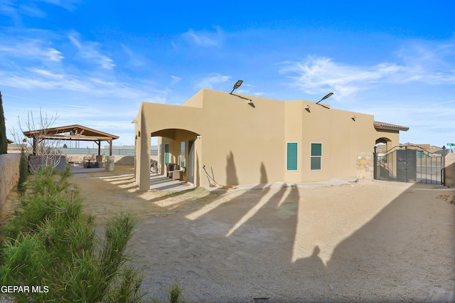 back of house with a gate, fence, a gazebo, and stucco siding