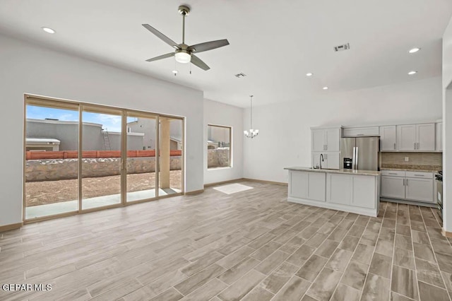 unfurnished living room featuring light wood-style floors, visible vents, baseboards, and ceiling fan with notable chandelier