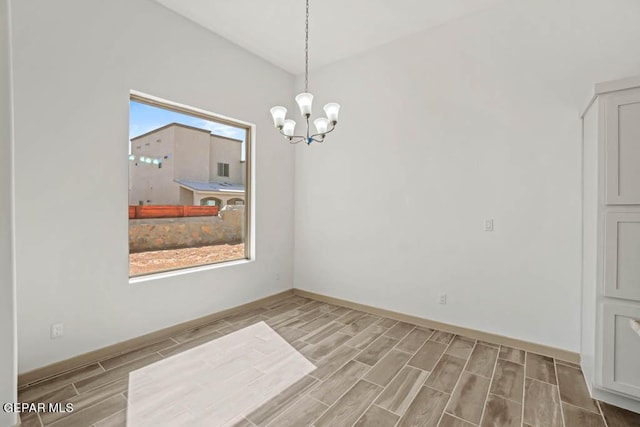 empty room featuring an inviting chandelier, wood tiled floor, and baseboards