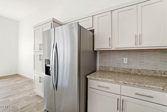 kitchen with wood finish floors, backsplash, white cabinets, light stone countertops, and stainless steel fridge