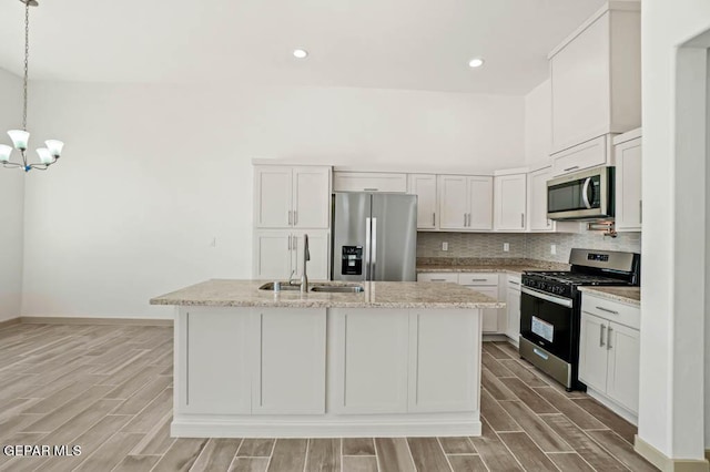 kitchen featuring decorative light fixtures, stainless steel appliances, a kitchen island with sink, white cabinets, and a sink