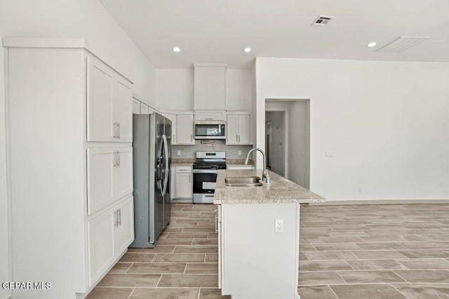 kitchen featuring a center island with sink, visible vents, stainless steel appliances, white cabinetry, and a sink