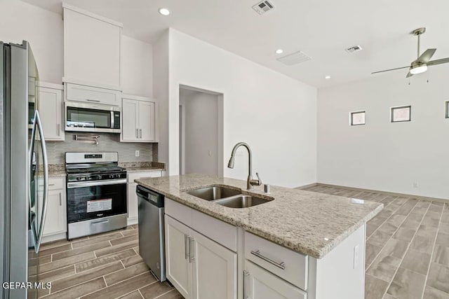 kitchen featuring stainless steel appliances, visible vents, a kitchen island with sink, a sink, and light stone countertops