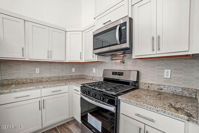 kitchen featuring tasteful backsplash, white cabinets, appliances with stainless steel finishes, light stone counters, and wood finished floors