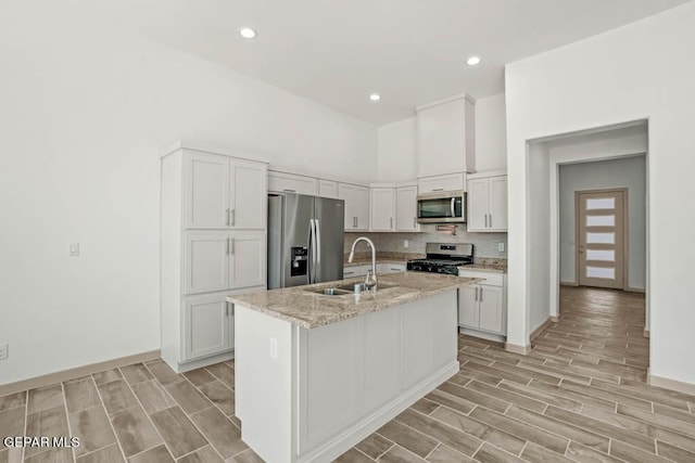 kitchen featuring light stone counters, stainless steel appliances, a sink, white cabinets, and a center island with sink