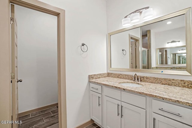 full bathroom featuring a shower with shower door, wood tiled floor, baseboards, and vanity