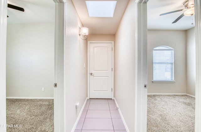 hallway with a skylight, tile patterned flooring, carpet flooring, and baseboards