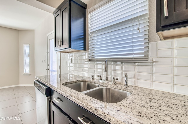 kitchen featuring backsplash, stainless steel dishwasher, light tile patterned flooring, a sink, and light stone countertops