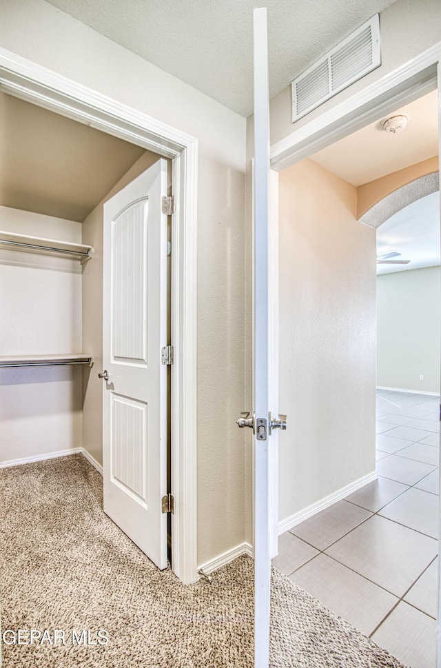 interior space with arched walkways, a textured ceiling, visible vents, baseboards, and carpet