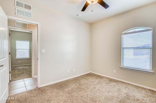 unfurnished room featuring a ceiling fan, light carpet, visible vents, and light tile patterned floors