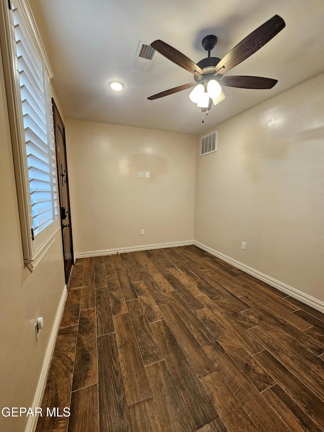 spare room featuring baseboards, visible vents, ceiling fan, and dark wood-style flooring