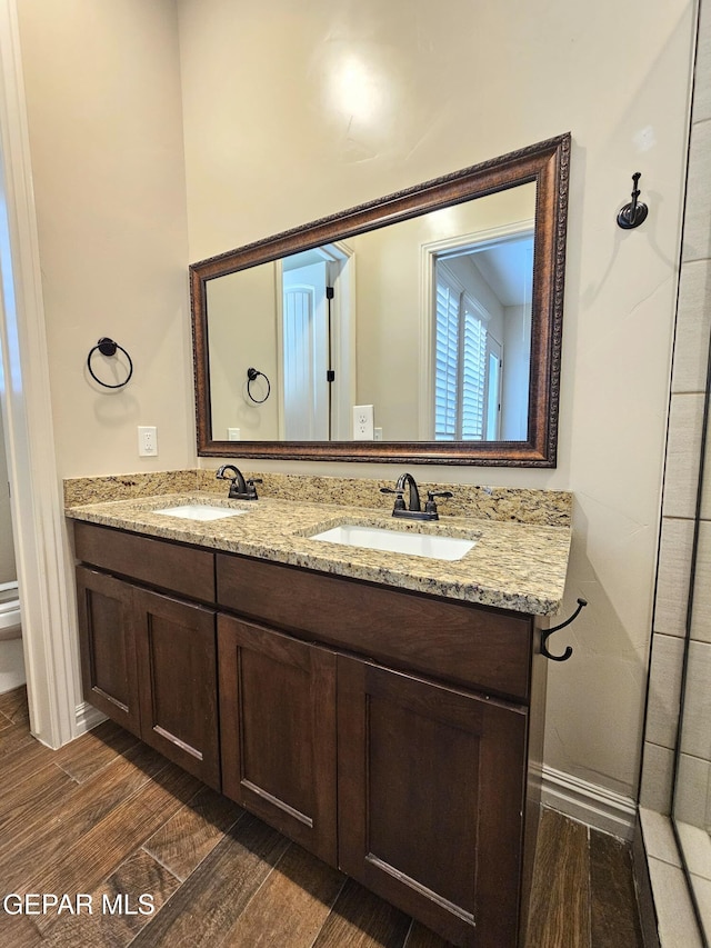 full bathroom featuring wood finish floors, a sink, baseboards, and double vanity