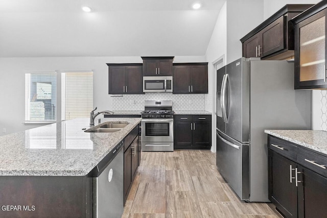 kitchen with light wood-style flooring, a sink, appliances with stainless steel finishes, a center island with sink, and glass insert cabinets