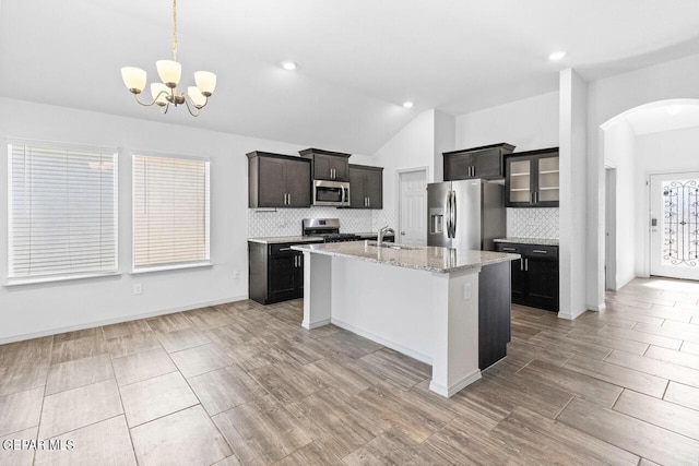 kitchen featuring arched walkways, stainless steel appliances, glass insert cabinets, a kitchen island with sink, and a sink