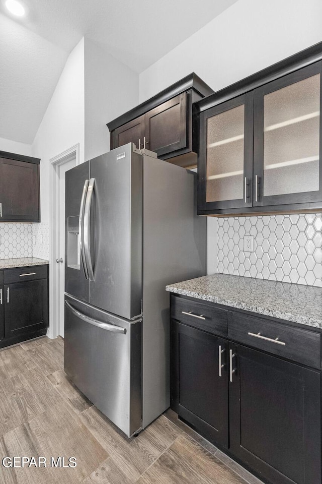 kitchen with decorative backsplash, glass insert cabinets, vaulted ceiling, light wood-type flooring, and stainless steel fridge with ice dispenser