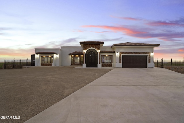 mediterranean / spanish-style home featuring an attached garage, driveway, fence, and stucco siding