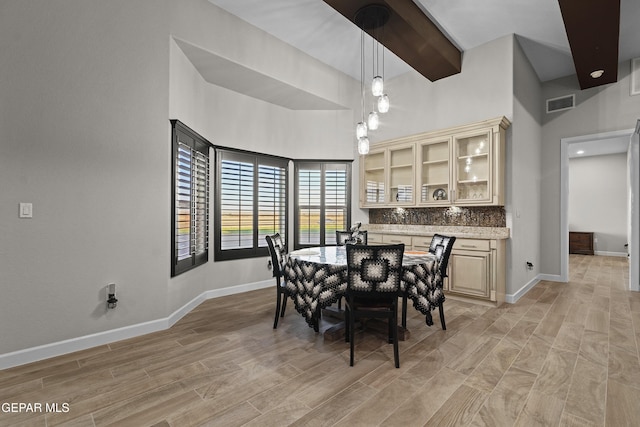 dining room with light wood-type flooring, baseboards, visible vents, and beamed ceiling