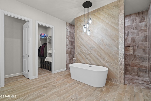 bathroom featuring wood finish floors, a freestanding tub, a spacious closet, and a walk in shower