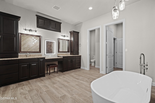 full bathroom featuring double vanity, visible vents, toilet, a freestanding bath, and a sink