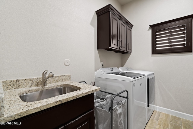 clothes washing area with washer and dryer, cabinet space, a sink, and baseboards