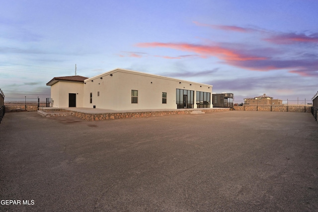 back of house at dusk with a patio, fence, and stucco siding