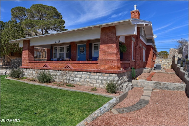 bungalow-style home with brick siding, a chimney, covered porch, fence, and a front lawn