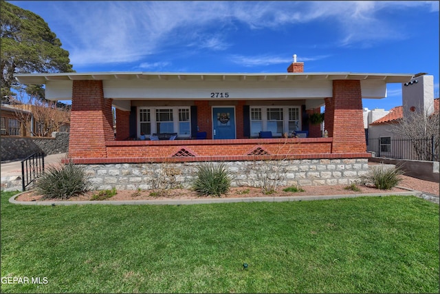 view of front of house with brick siding, a chimney, a front yard, and fence