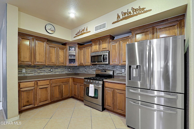 3537 Tierra Bahia Dr, El Paso, TX 79938 - kitchen with appliances with stainless steel finishes, brown cabinetry, visible vents, and light tile patterned flooring