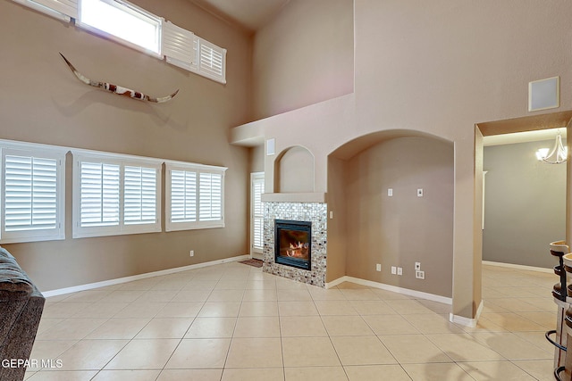 3537 Tierra Bahia Dr, El Paso, TX 79938 - living area with a notable chandelier, a towering ceiling, a tiled fireplace, light tile patterned flooring, and baseboards