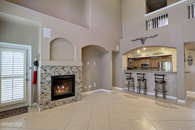3537 Tierra Bahia Dr, El Paso, TX 79938 - living room featuring arched walkways, light tile patterned flooring, a tile fireplace, and baseboards