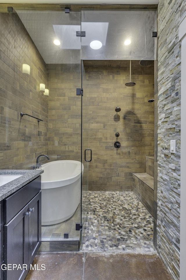 full bath with a stall shower, a freestanding tub, vanity, and tile walls