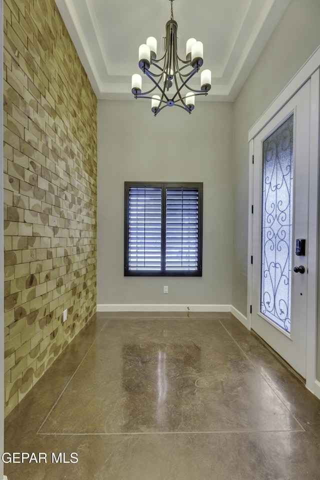 foyer entrance featuring concrete flooring, a tray ceiling, a notable chandelier, and brick wall