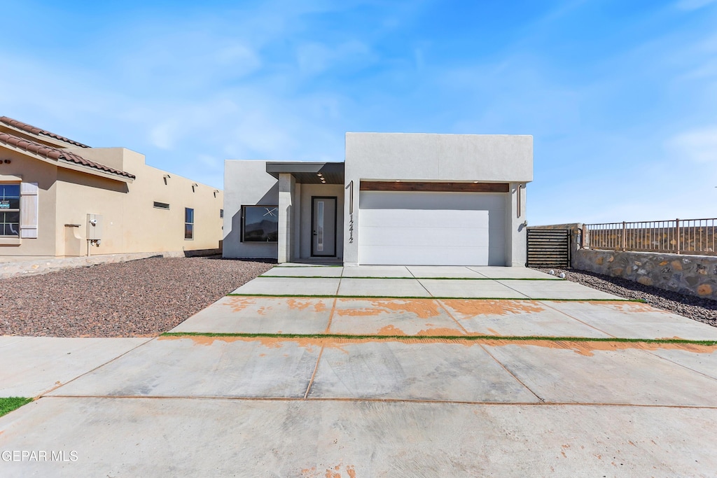 view of front of property with a garage, concrete driveway, fence, and stucco siding