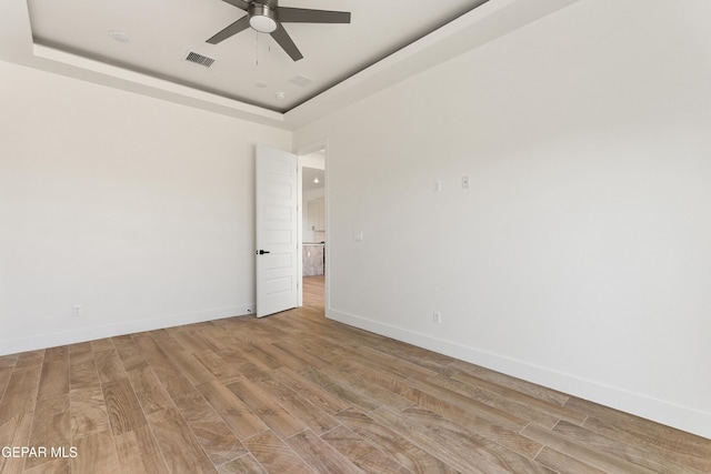 unfurnished room featuring light wood-style flooring, a raised ceiling, visible vents, and baseboards