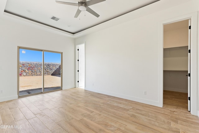 empty room with baseboards, light wood-style flooring, visible vents, and a tray ceiling