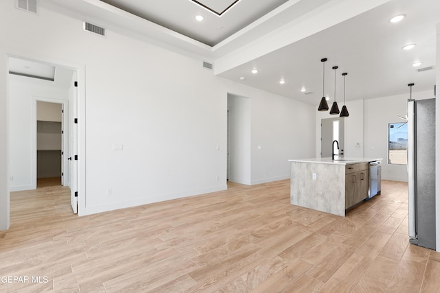 kitchen with a center island with sink, visible vents, light countertops, hanging light fixtures, and a sink