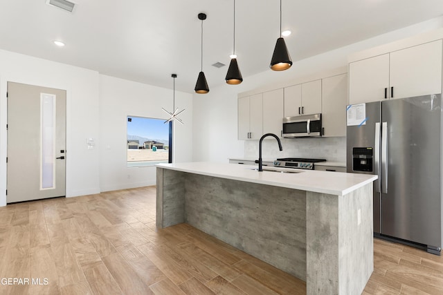 kitchen with stainless steel appliances, an island with sink, light countertops, and white cabinetry