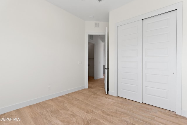 unfurnished bedroom featuring a closet, baseboards, visible vents, and light wood finished floors