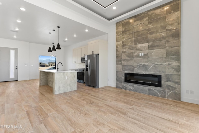 kitchen with stainless steel appliances, open floor plan, hanging light fixtures, light countertops, and a center island with sink