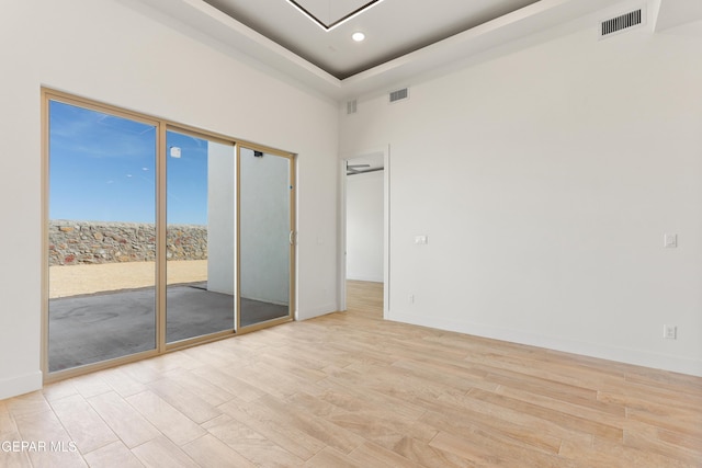 unfurnished room with light wood-type flooring, a raised ceiling, and visible vents