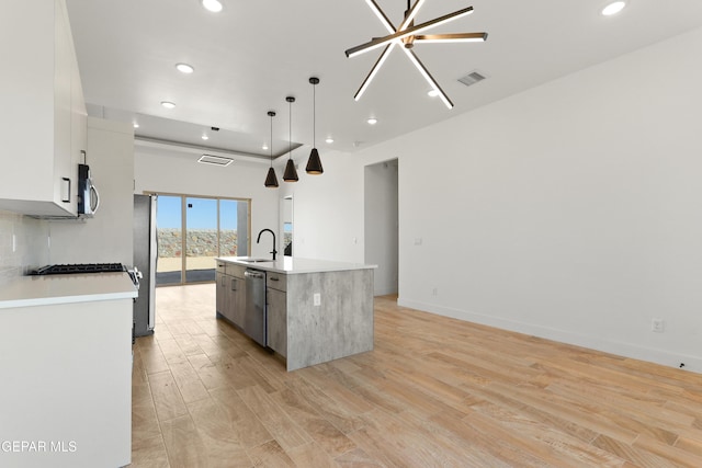 kitchen featuring a center island with sink, visible vents, decorative light fixtures, light countertops, and white cabinetry