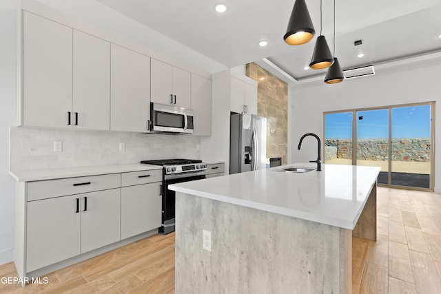 kitchen featuring a sink, hanging light fixtures, appliances with stainless steel finishes, light countertops, and an island with sink