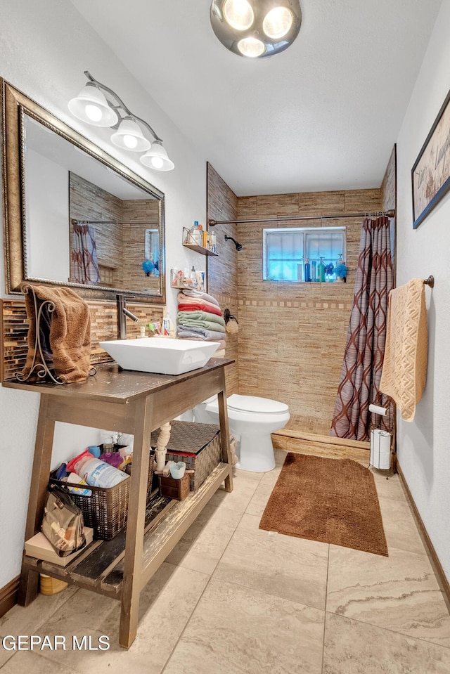 full bath featuring tiled shower, a sink, toilet, and baseboards